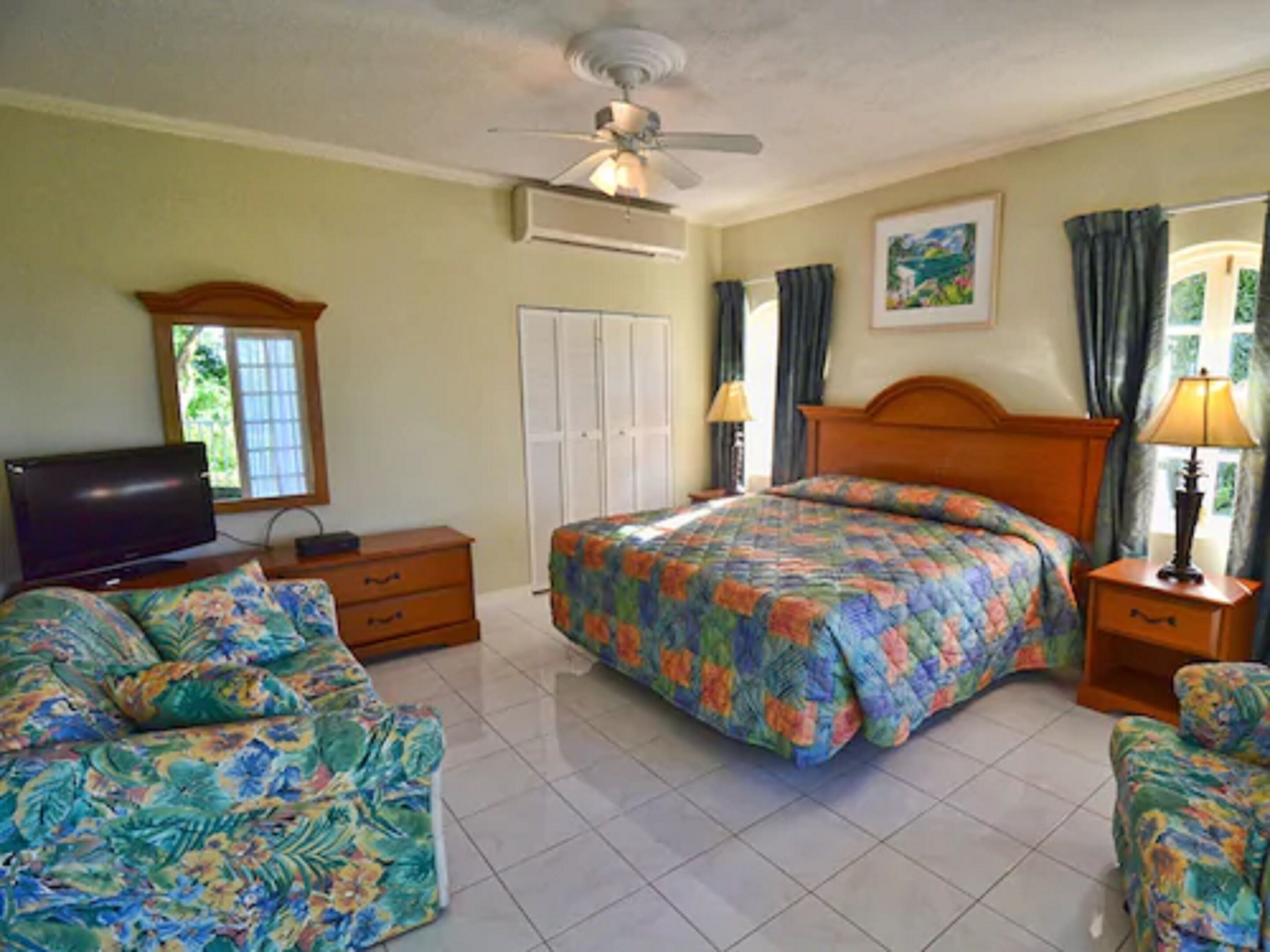 Une chambre à coucher comprenant un lit, une télévision, une commode, une armoire et un ventilateur de plafond.