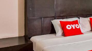 A hotel room with a dark headboard, a bed with white bedding and red pillows, and a small decorative item on the wall.