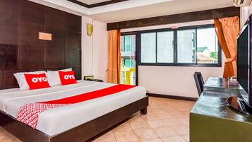A hotel room with a large bed, a desk with a television, and a window with curtains.