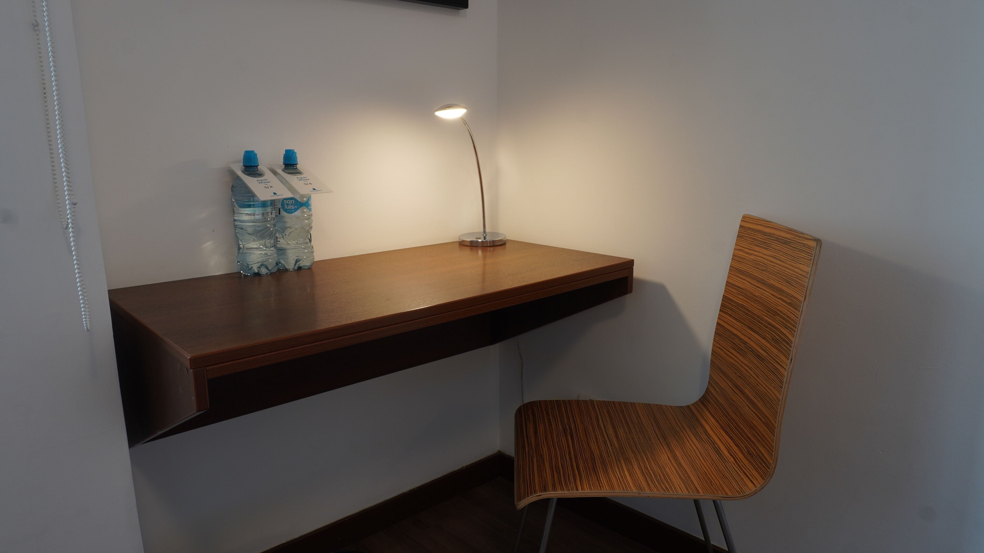 A wooden desk with two water bottles and a desk lamp.