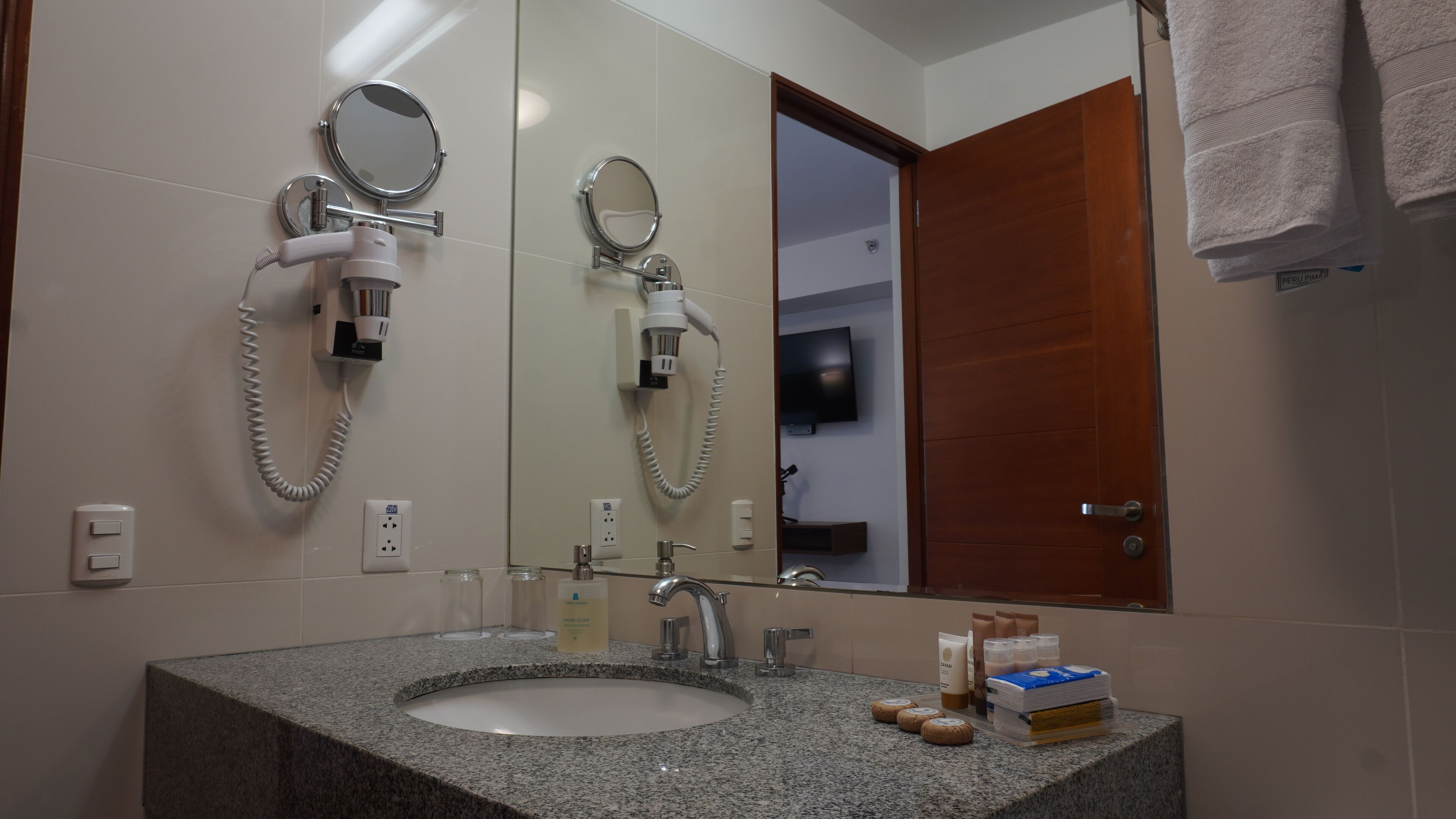 A bathroom with a granite sink, two mirrors, a hairdryer, and a towel rack.