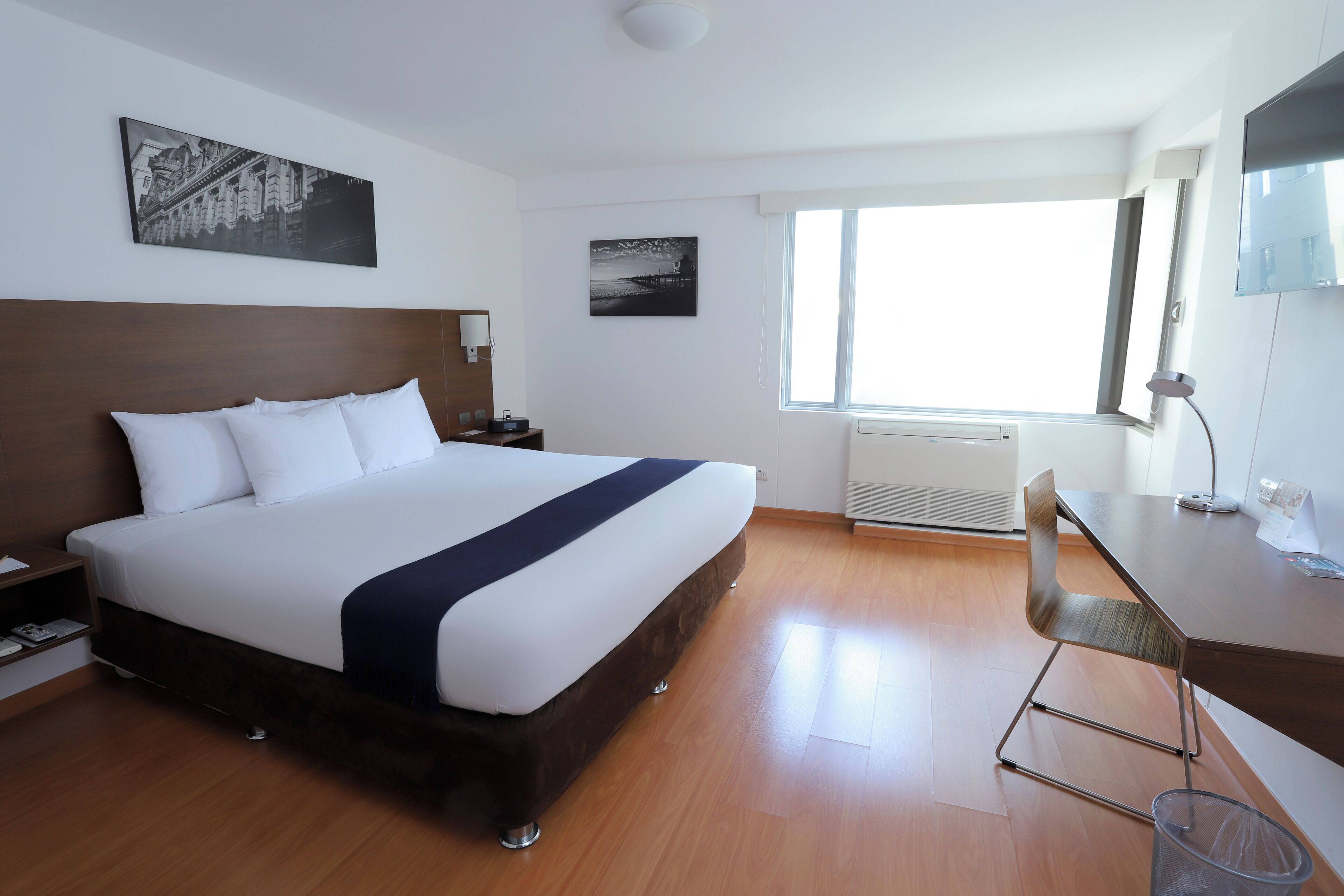 A hotel room with a large bed, a desk, a chair, a nightstand, and two wall-mounted lamps.
