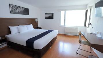 A hotel room with a large bed, a desk, a chair, a nightstand, and two wall-mounted lamps.