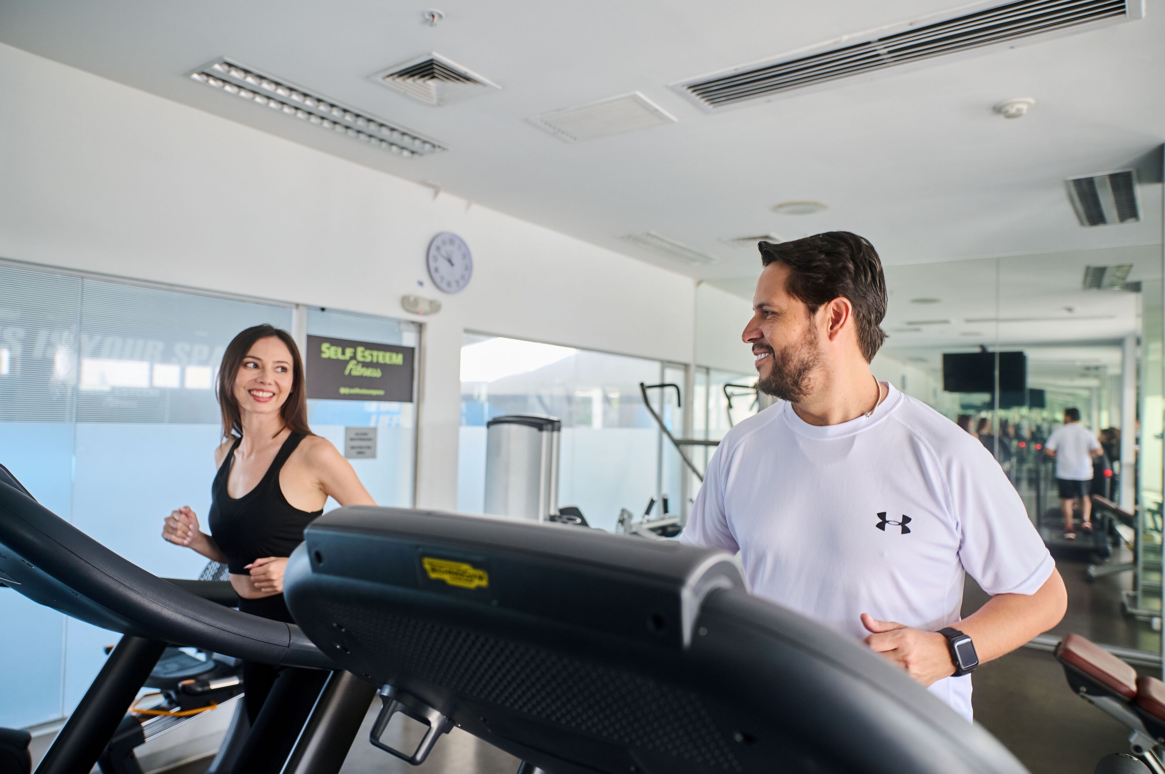 Une salle de sport équipée de tapis de course, d’une horloge et d’une enseigne sur laquelle on peut lire : « SELF ESTERM Fitness ».