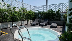 Un área de piscina en la azotea con un jacuzzi, sillas de descanso y una valla de celosía blanca.
