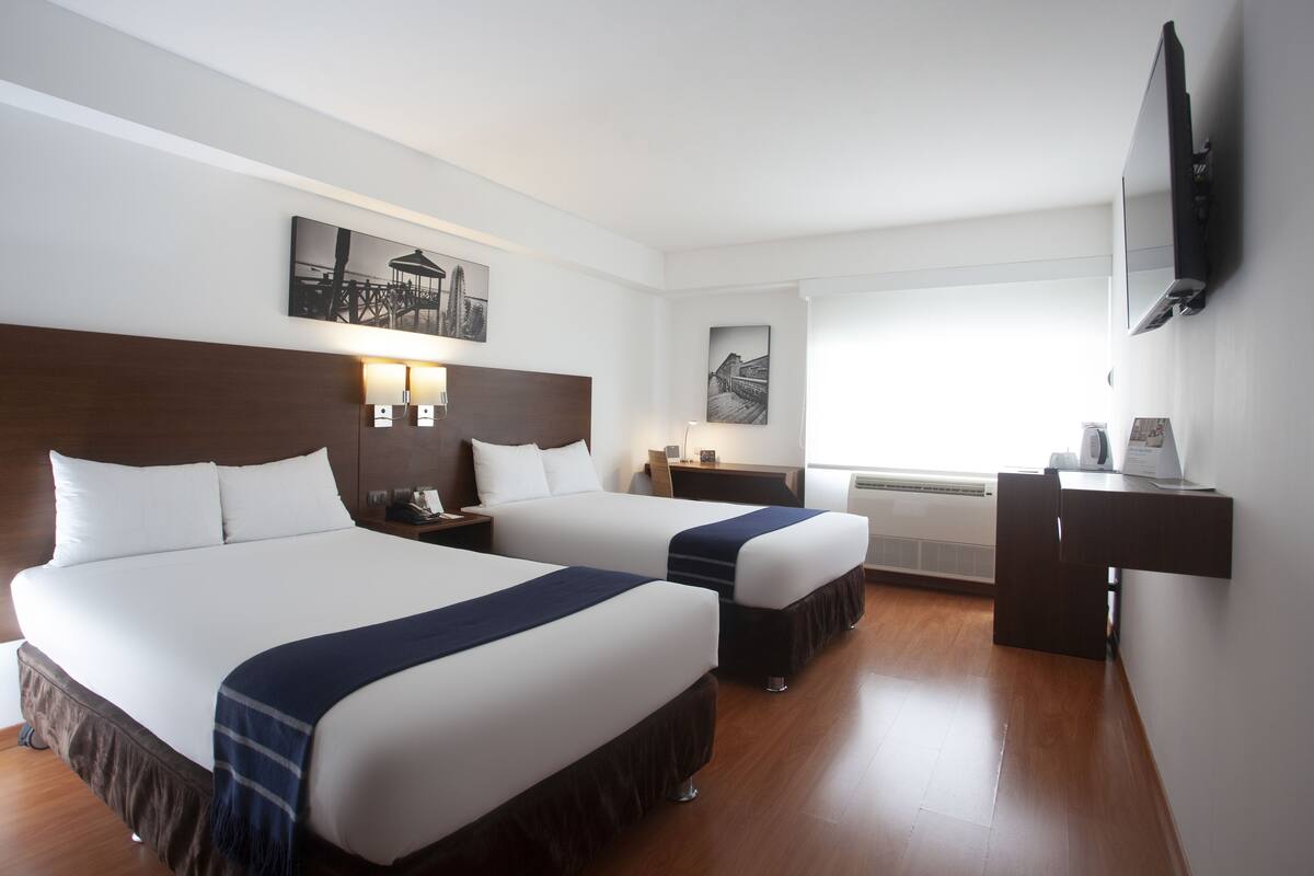 Habitación de hotel con dos camas, un escritorio, un televisor y obras de arte en las paredes.