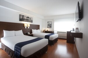 A hotel room with two beds, a desk, a TV, and artwork on the walls.