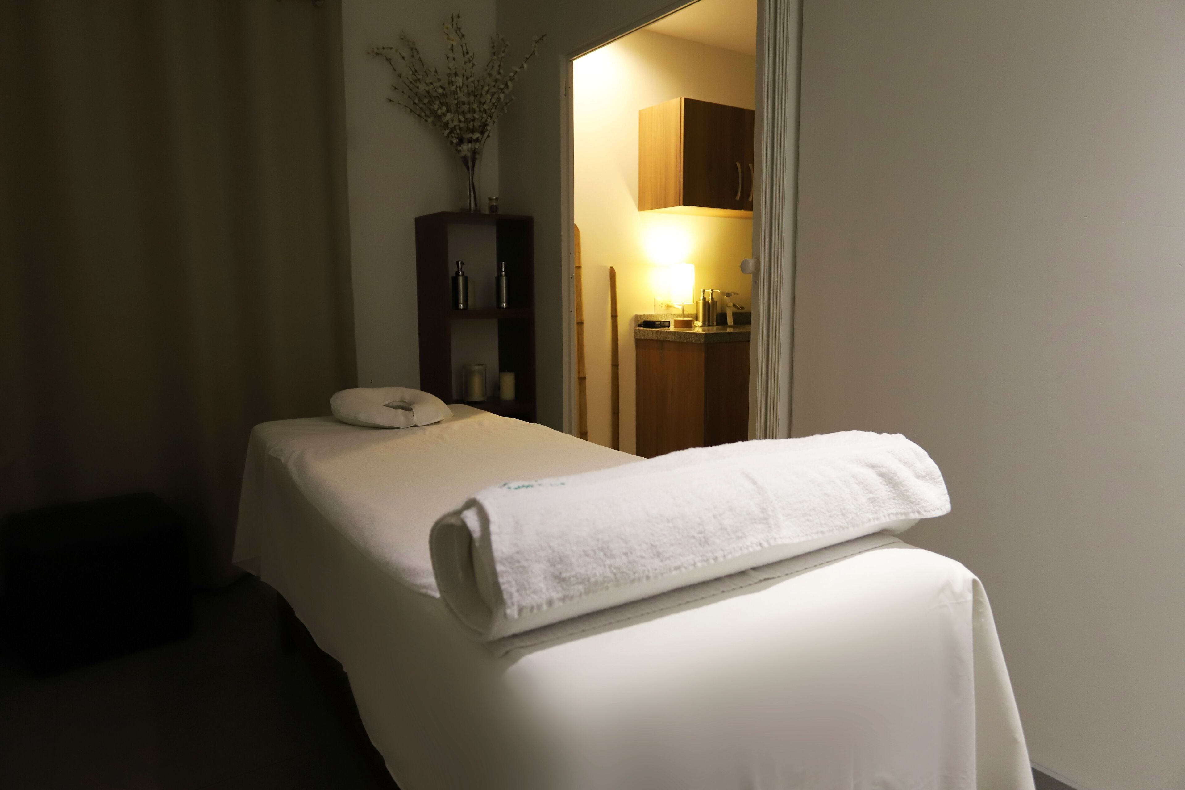 Hotellihuone, jossa on siististi pedattu sänky, pieni kaappi hygieniatarvikkeille ja ovi, joka johtaa kylpyhuoneeseen.