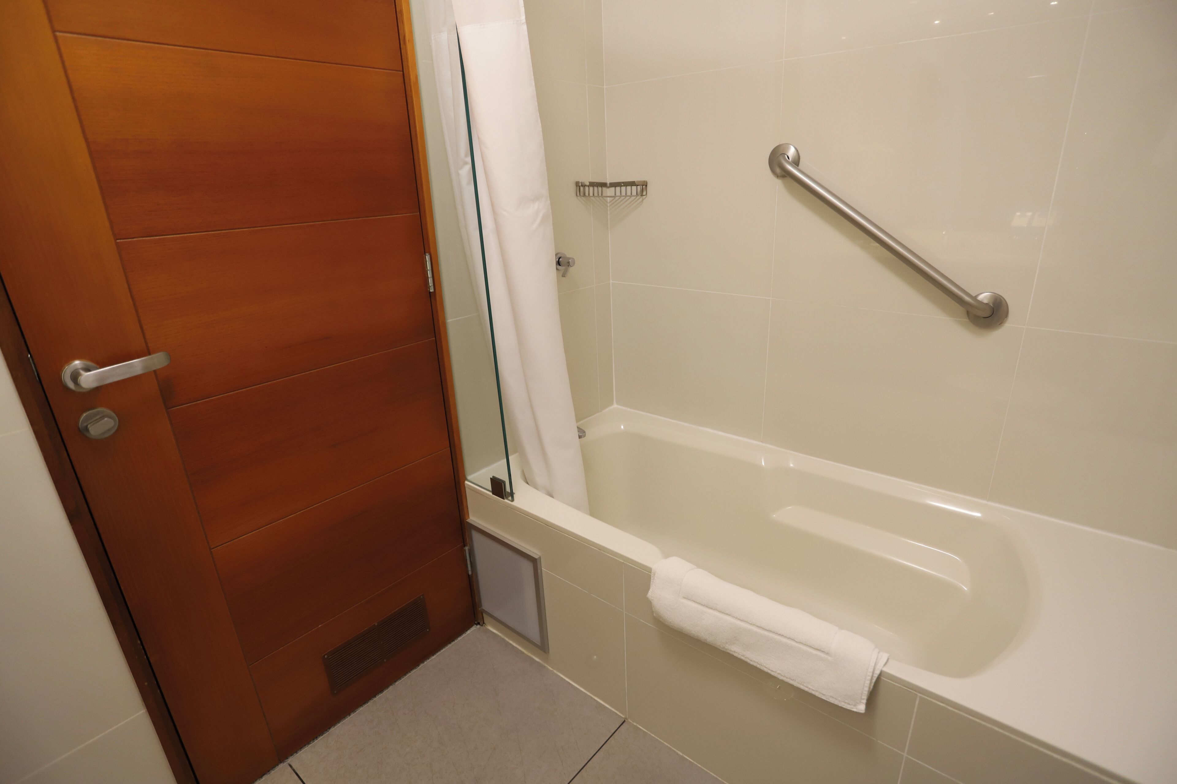 A bathroom with a wooden door, a white bathtub, and a handrail.