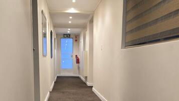 A hotel hallway with a striped carpet, white walls, and a window with blinds.