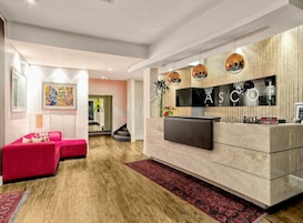 Un moderno vestíbulo de hotel con mostrador de recepción, un espejo grande y un cuadro abstracto colorido.