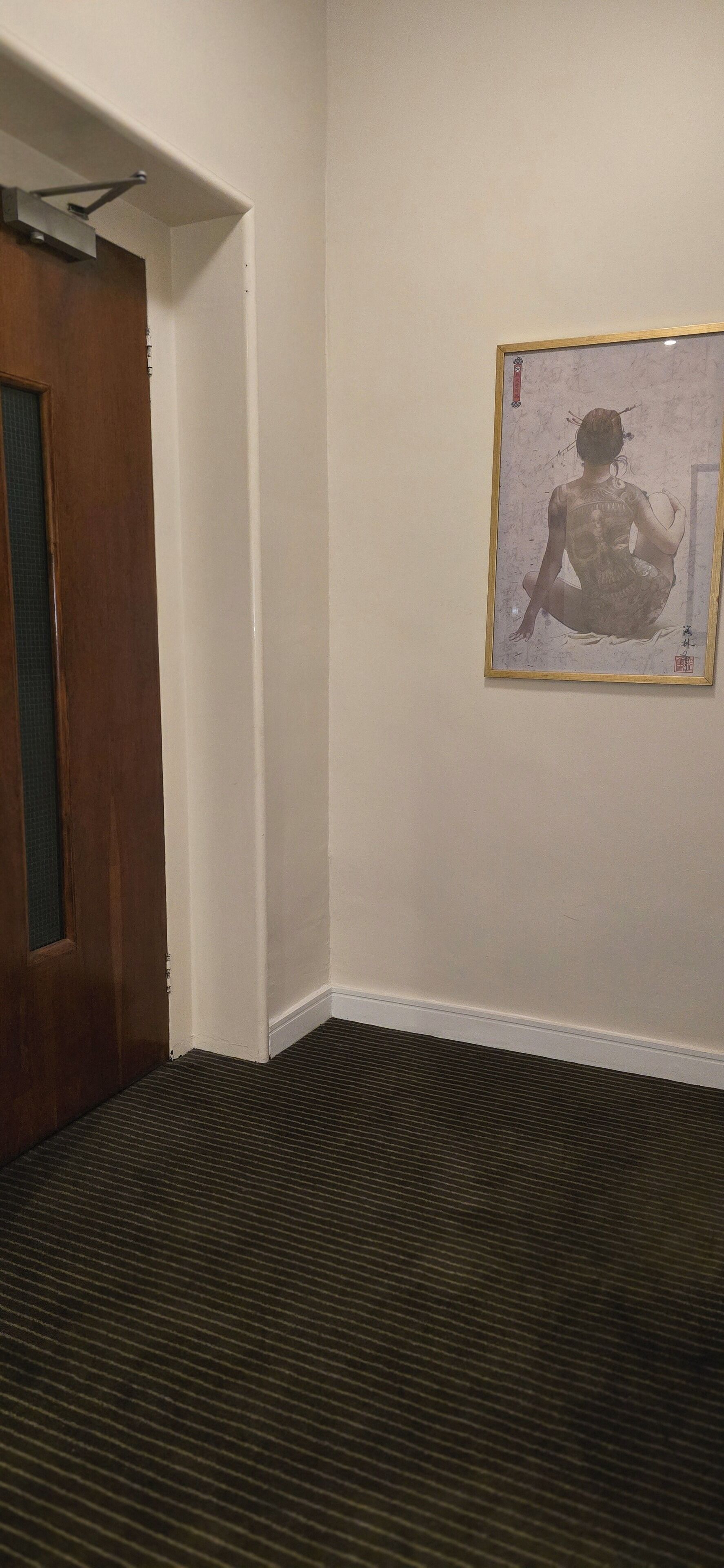 Una habitación de esquina con una puerta de madera, una obra de arte enmarcada en la pared y una alfombra estampada.