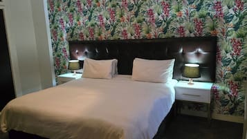 Een hotelkamer met een bed, twee nachtkastjes met lampen en bloemenbehang.