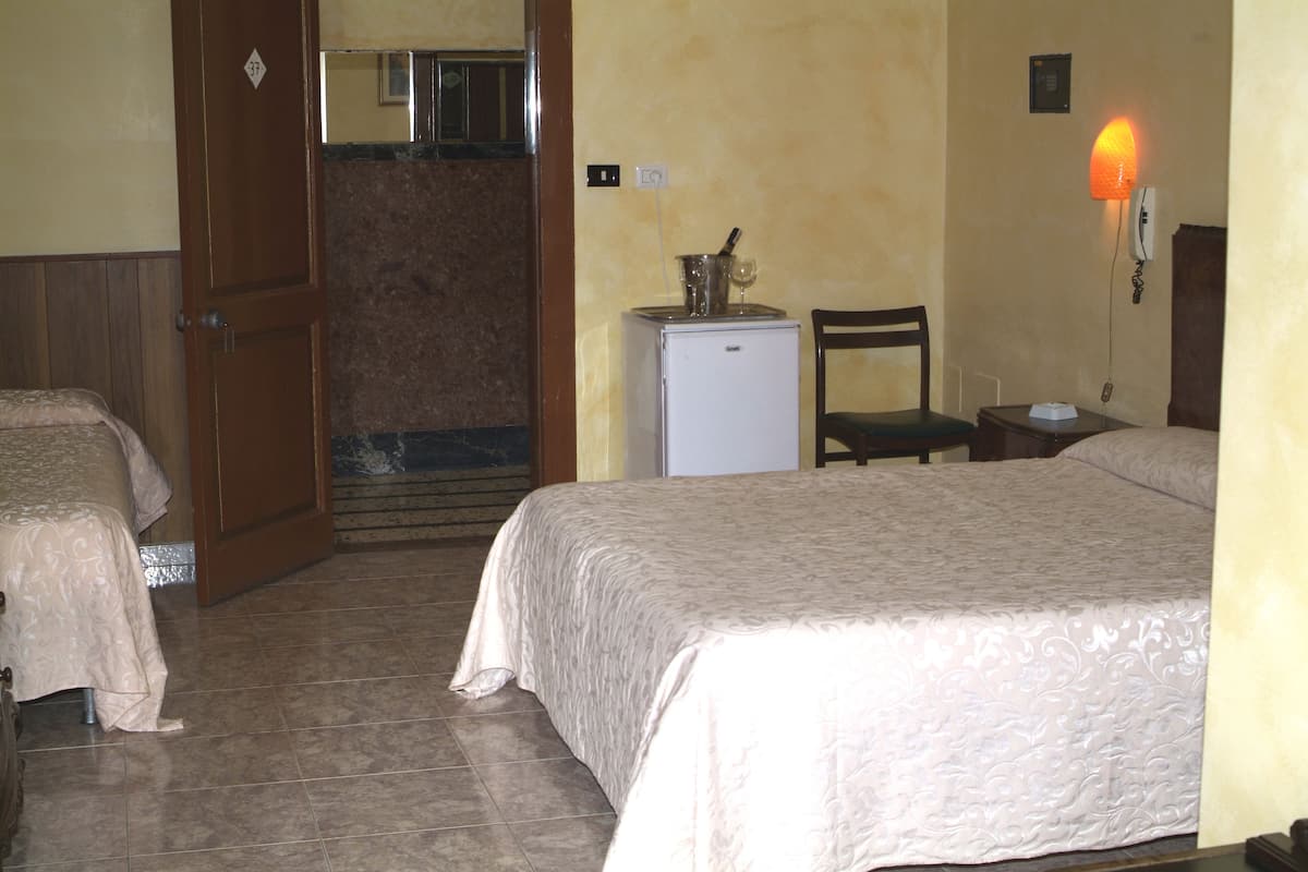 A hotel room with two beds, a small refrigerator, a chair, and a wall-mounted phone.