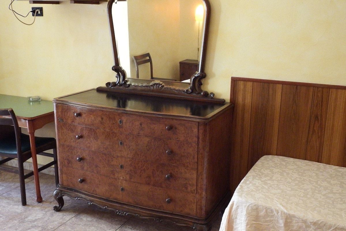 A wooden dresser with a mirror, a chair, and a bed with a patterned bedspread.