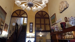 A grand hallway with a crystal chandelier, arched doorways, a clock, and a staircase leading to another floor. - Hotel Touring (Messina)
