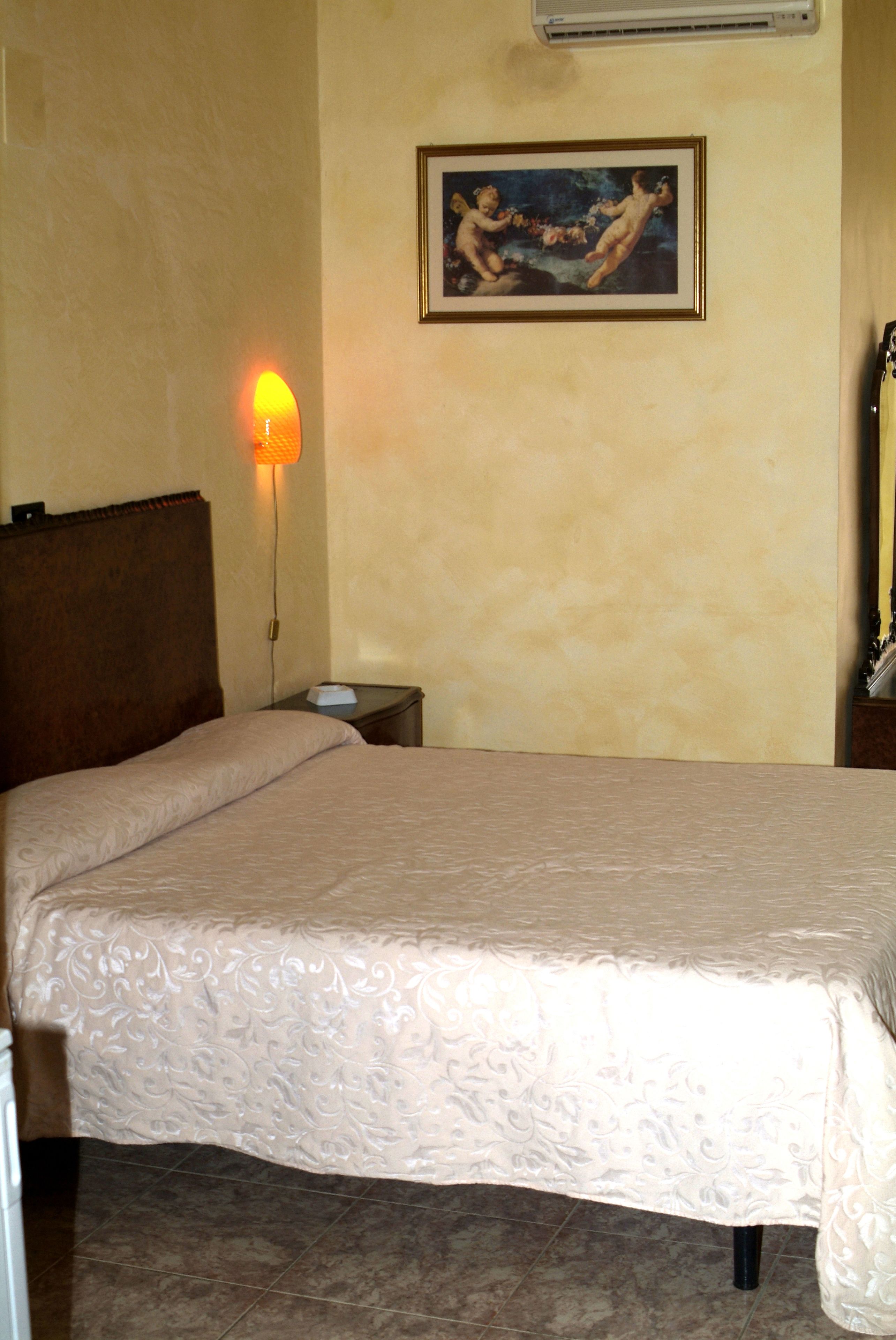 A hotel room with a bed, a nightstand, a lamp, and a painting on the wall.