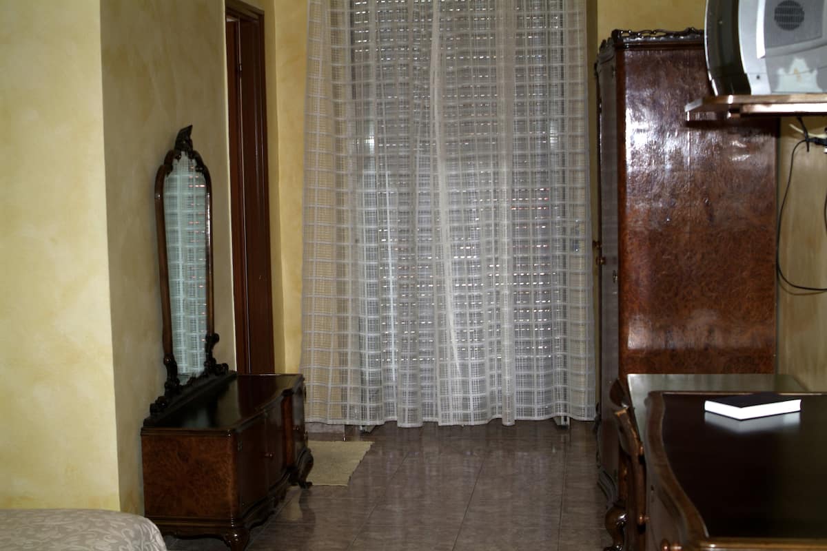 A room with a wooden dresser, a mirror, a bed, and a television on a wooden stand.