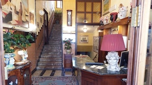 A staircase with a wooden railing, a patterned carpet, and a desk with a lamp and decorative items. - Hotel Touring (Messina)
