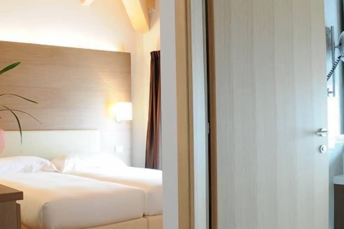 A hotel room with two beds, a nightstand, a vase with flowers, and a door with a telephone.
