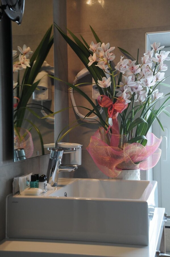 Un baño con un lavamanos blanco, un espejo y un jarrón de flores.