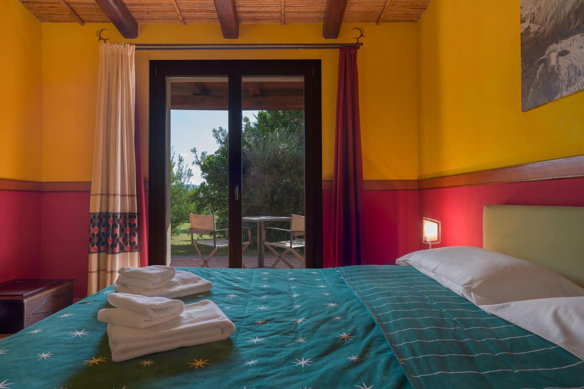 A hotel room with a bed, a table, chairs, and a view of the outdoors.