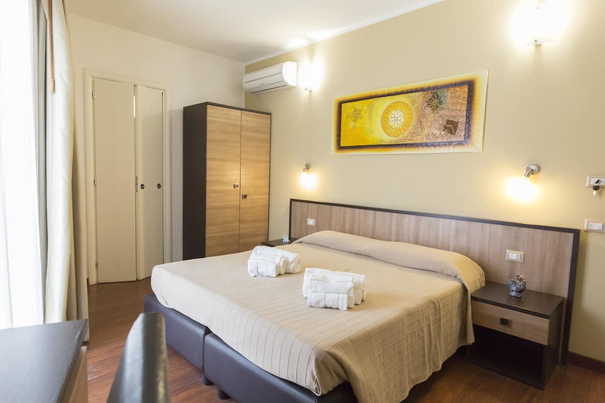 Ein Hotelzimmer mit Bett, Nachttisch, Schreibtisch, Kleiderschrank und einem Gemälde an der Wand.