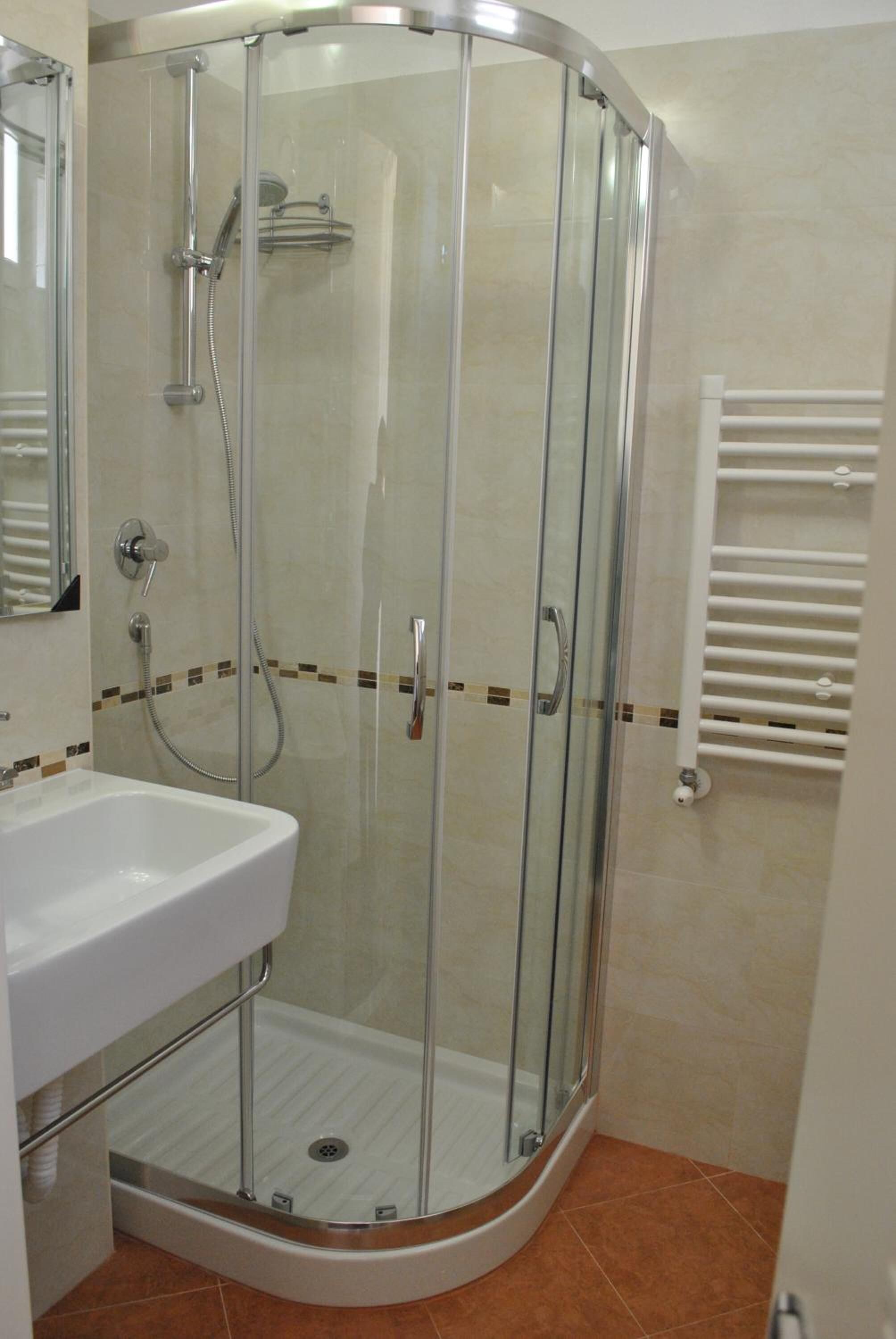 A glass-enclosed shower stall with a white sink and a towel rack.