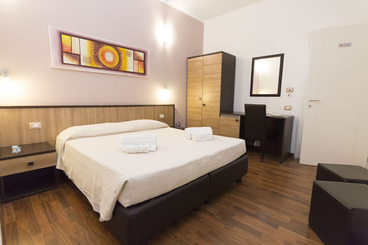 Ein Hotelzimmer mit einem großen Bett, einem Schreibtisch, einem Kleiderschrank und einem Spiegel.
