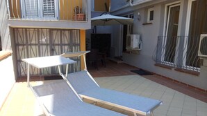 A sunlit outdoor patio with two lounge chairs and a table, a small table, and a potted plant. - Lewisrooms Domo (Cagliari)
