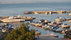 A marina with various boats docked, a lighthouse in the background, and a cyclist on the path. - Lewisrooms Domo (Cagliari)