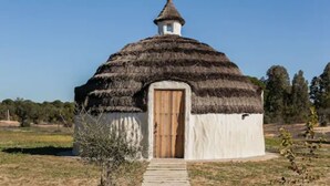 Una estructura tradicional con techo de paja, puerta de madera y una pequeña torre en la parte superior.