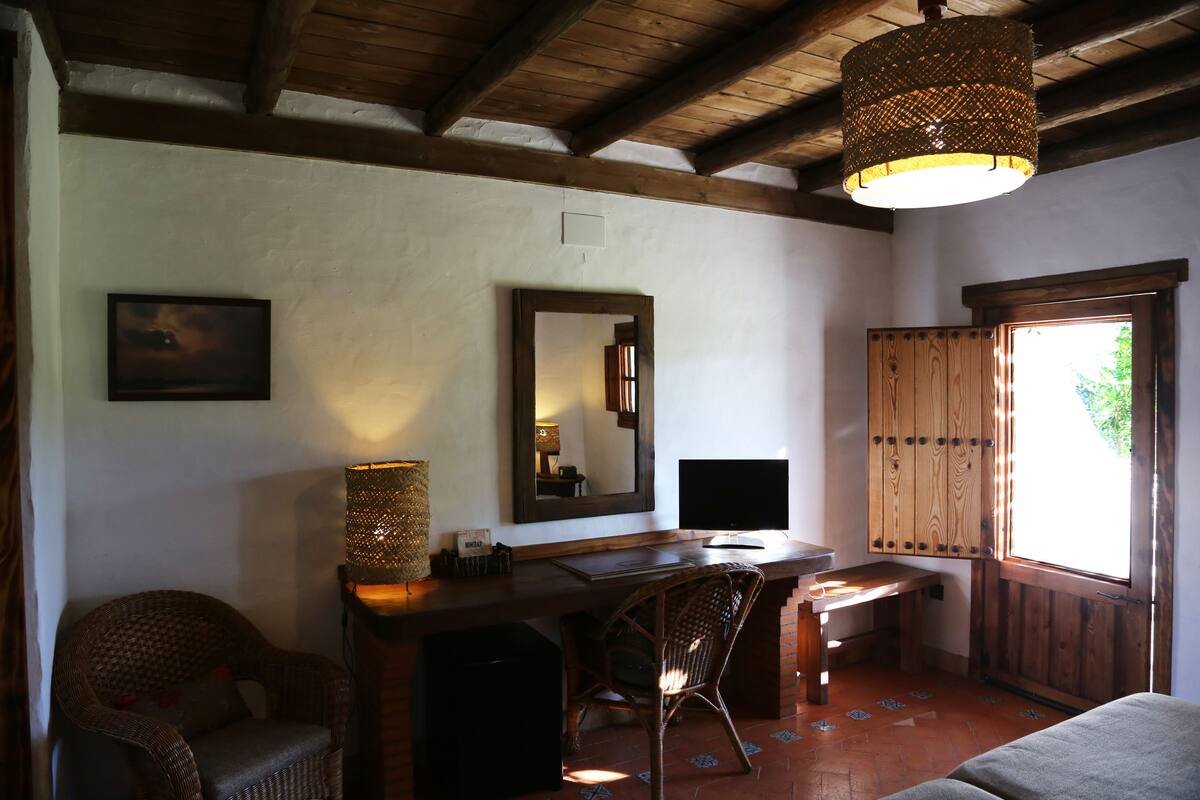 A rustic room with a wooden desk, a chair, a large mirror, and a window with wooden shutters.