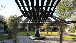 Un patio con una fuente de piedra, un pérgola de madera y un edificio al fondo.