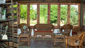 Un porche de madera con mobiliario de mimbre, una mesa con un florero y vistas a árboles.