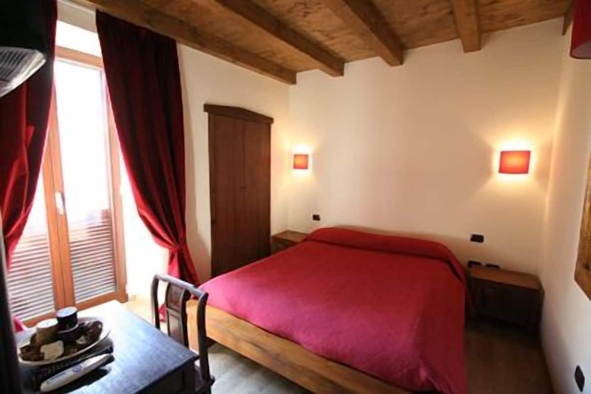 Een slaapkamer met een houten bed, rode gordijnen, een houten tafel met een stoel en twee bedlampen.