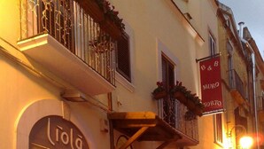 Ein Hotelzugang mit rotem Teppich, einem Schild mit der Aufschrift "L'Ioia" und einer Person rechts.
