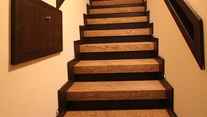 Eine Treppe mit hölzernem Geländer und Teppichstufen, die zu einer Empore führen.