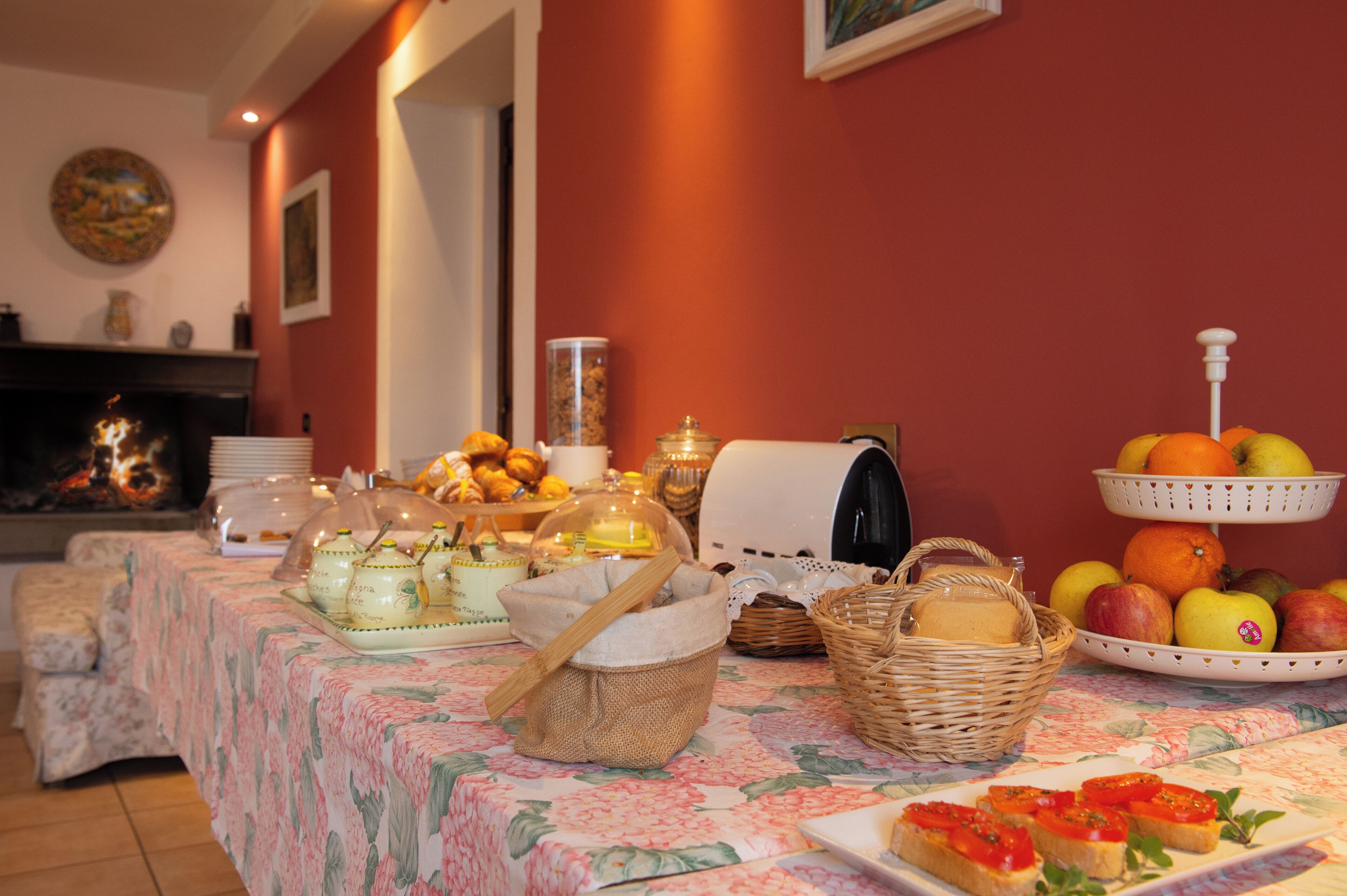 A breakfast buffet with various food items, a fireplace, and a floral tablecloth.