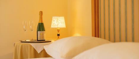 Habitación de hotel con cama, mesita de noche con una botella de champán, dos copas y una lámpara de mesa.