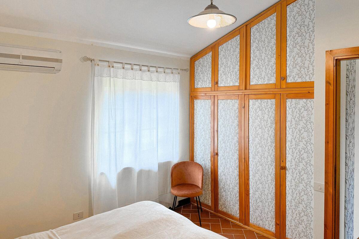 Quarto com cama, cadeira, guarda-roupa e janela com cortinas.