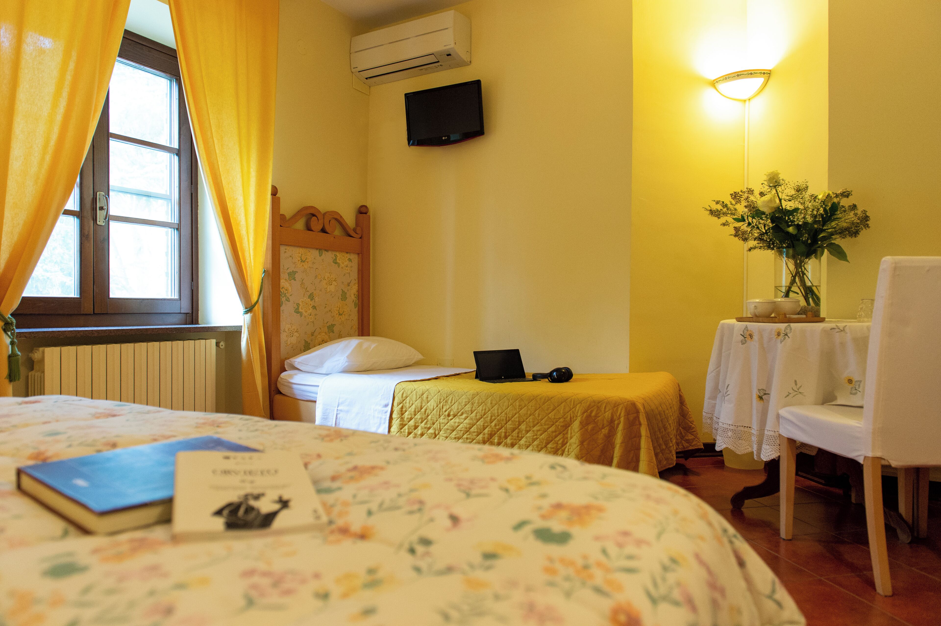 Ein Hotelzimmer mit einem Bett, einem Schreibtisch mit einem Laptop, einem Sessel, einem Tisch mit einer Vase und einem wandmontierten Fernseher.