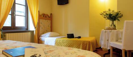 Ein Hotelzimmer mit einem Bett, einem Schreibtisch mit einem Laptop, einem Sessel, einem Tisch mit einer Vase und einem wandmontierten Fernseher.