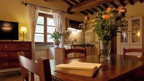 A wooden dining table with chairs, a vase of flowers, a book, and a television on a wooden cabinet. - Podere Sette Piagge (Orvieto)