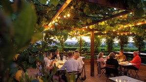 An outdoor dining area with tables under a pergola covered with vines, string lights, and a view of the landscape. - Podere Sette Piagge (Orvieto)