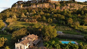 A villa with a swimming pool, surrounded by lush greenery and a cliff with a tower. - Podere Sette Piagge (Orvieto)