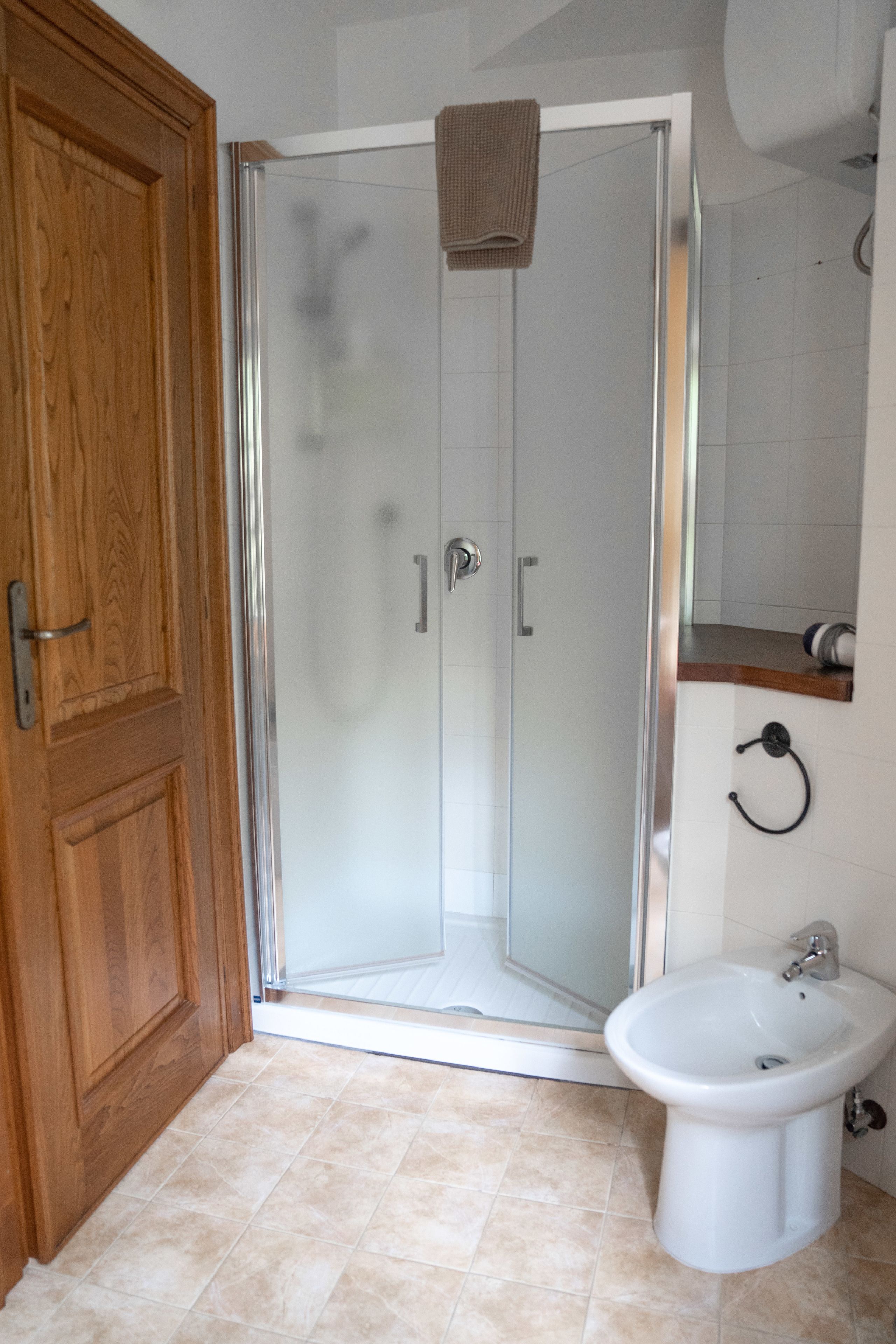 Un baño con cabina de ducha de vidrio, puerta de madera, lavamanos blanco y una toalla colgada en la puerta de la ducha.