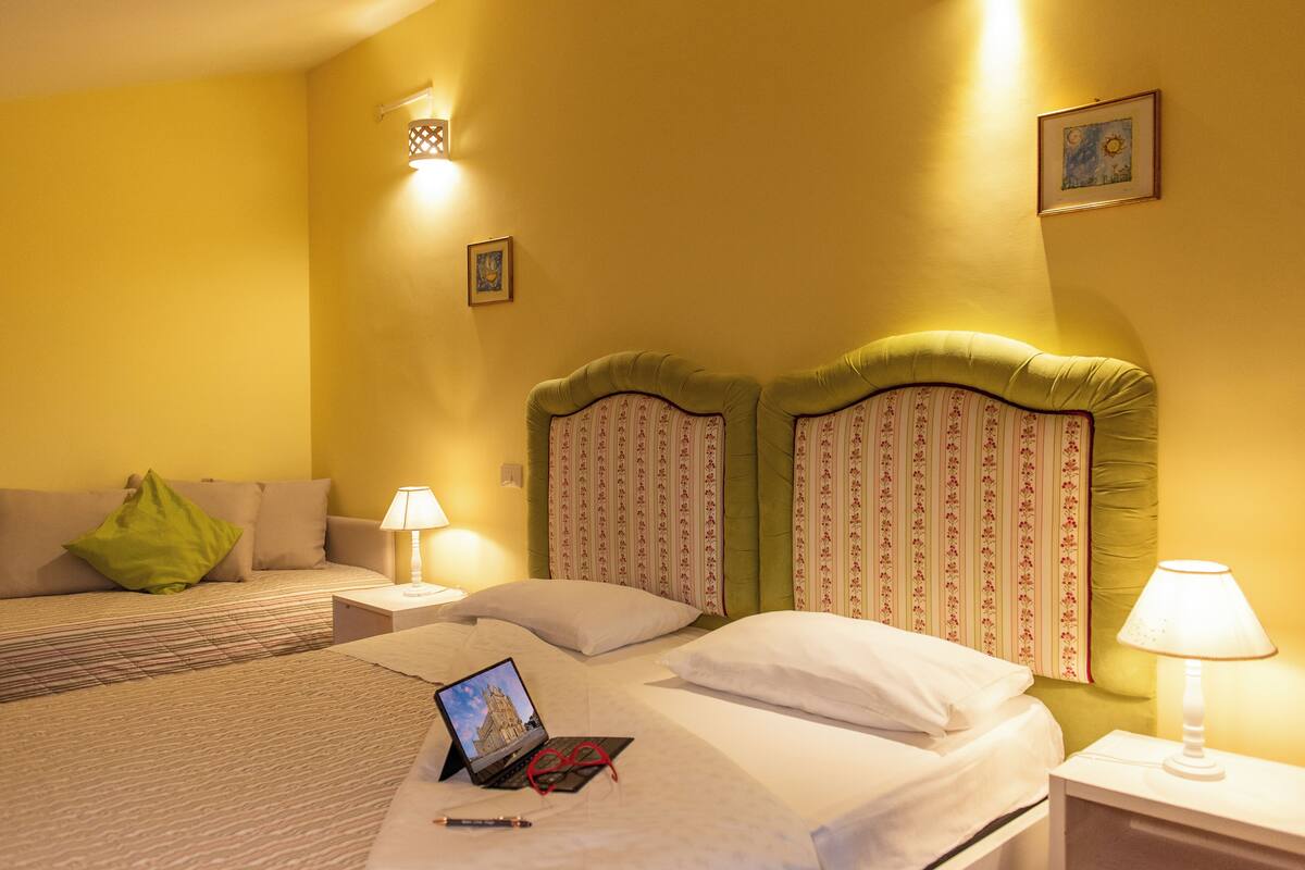 Quarto de hotel com uma cama, mesa de cabeceira, abajur e um laptop sobre a cama.