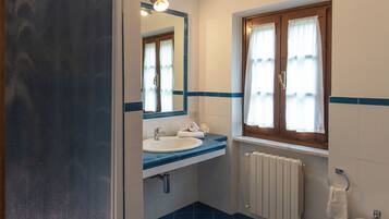 Ein Badezimmer mit Waschbecken, Spiegel, Fenster mit Vorhängen und Heizkörper.