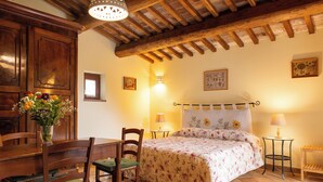 A bedroom with a wooden ceiling, a bed with floral bedding, a dining table with chairs, and a vase with flowers. - Podere Sette Piagge (Orvieto)